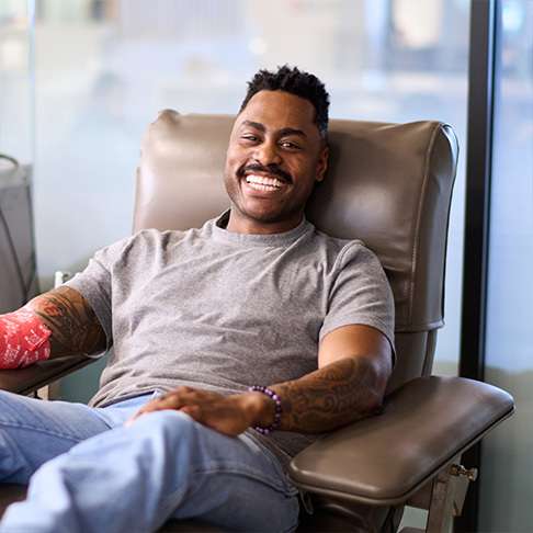 Black man with a grey shirt sitting in a donation chair with a red arm bandage