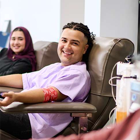 Man with a light purple shirt sitting in a donation chair with a red arm bandage