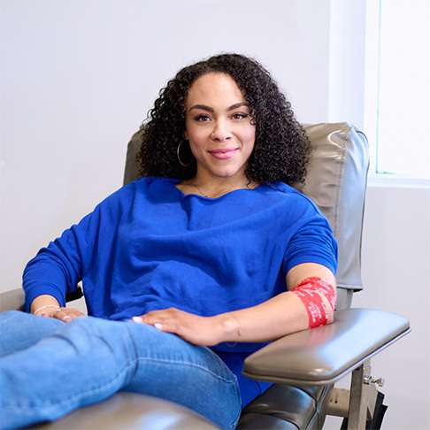Woman sitting in a donation chair in blue jean and blue shirt with a red arm bandage
