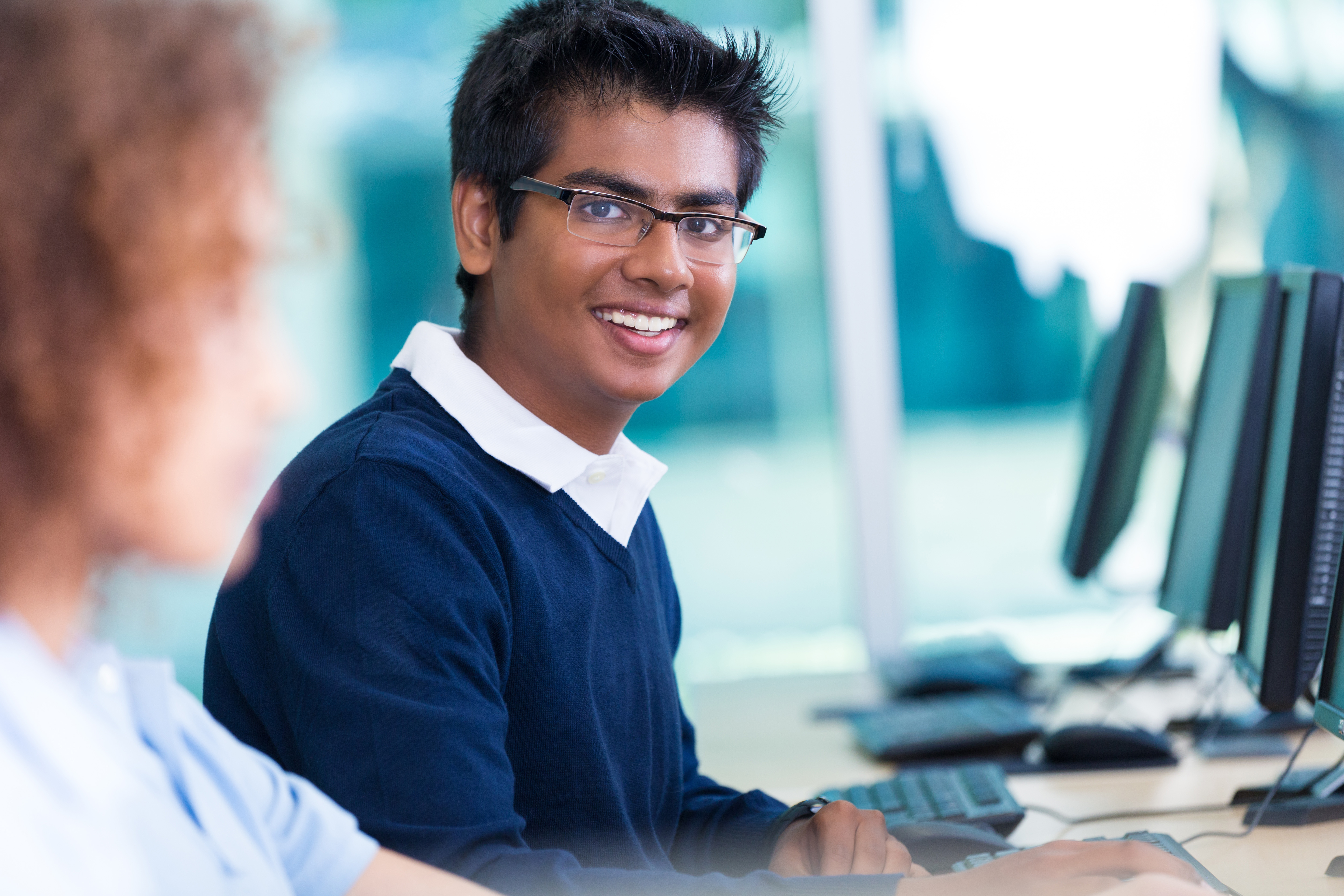 Male student smiling and sitting behind a computer 