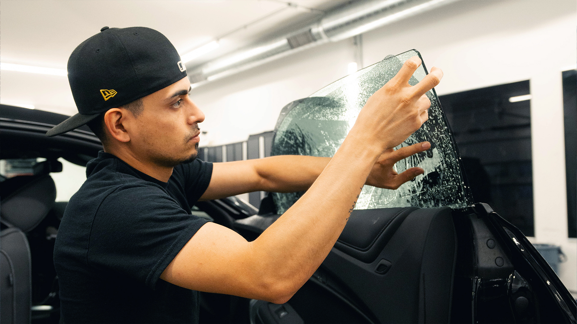 Technician fitting window tint film to a vehicle side window