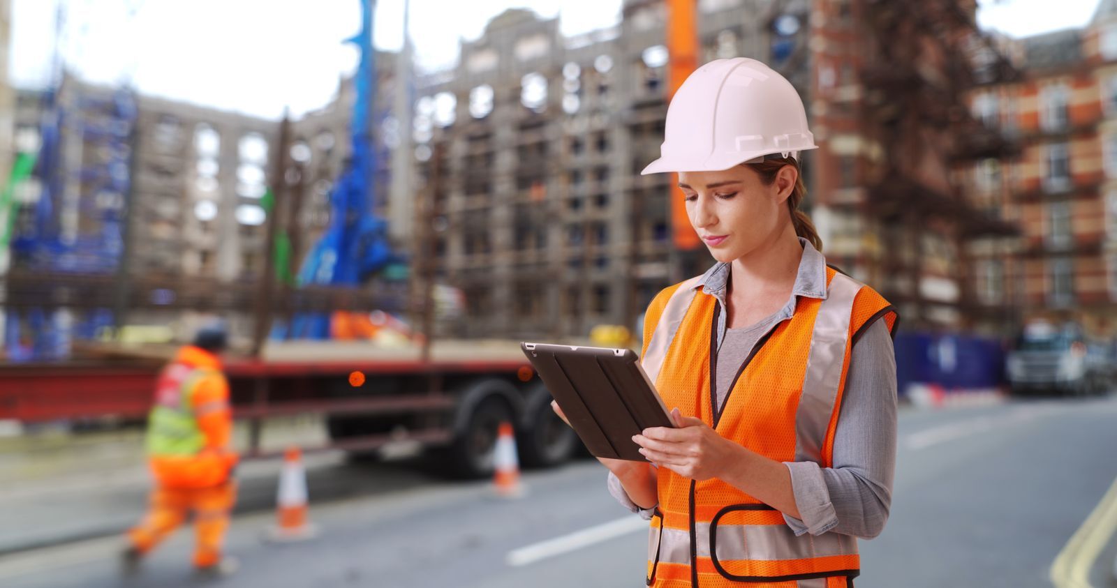 Construction safety professional in a hard hat reviewing a report on a tablet at a jobsite