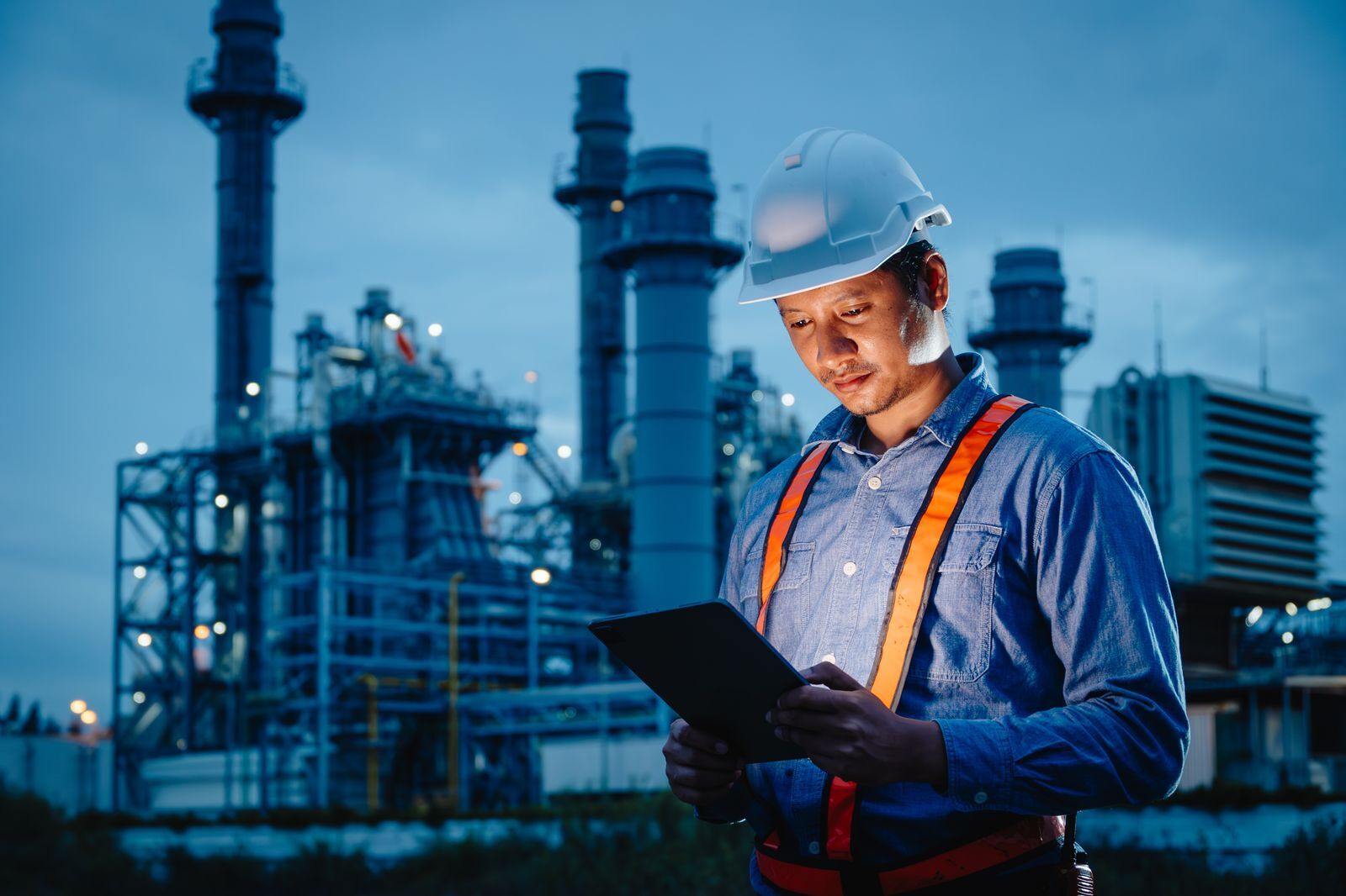Safety professional in a hard hat and high-visibility vest reviewing an inspection on a tablet at an energy facility