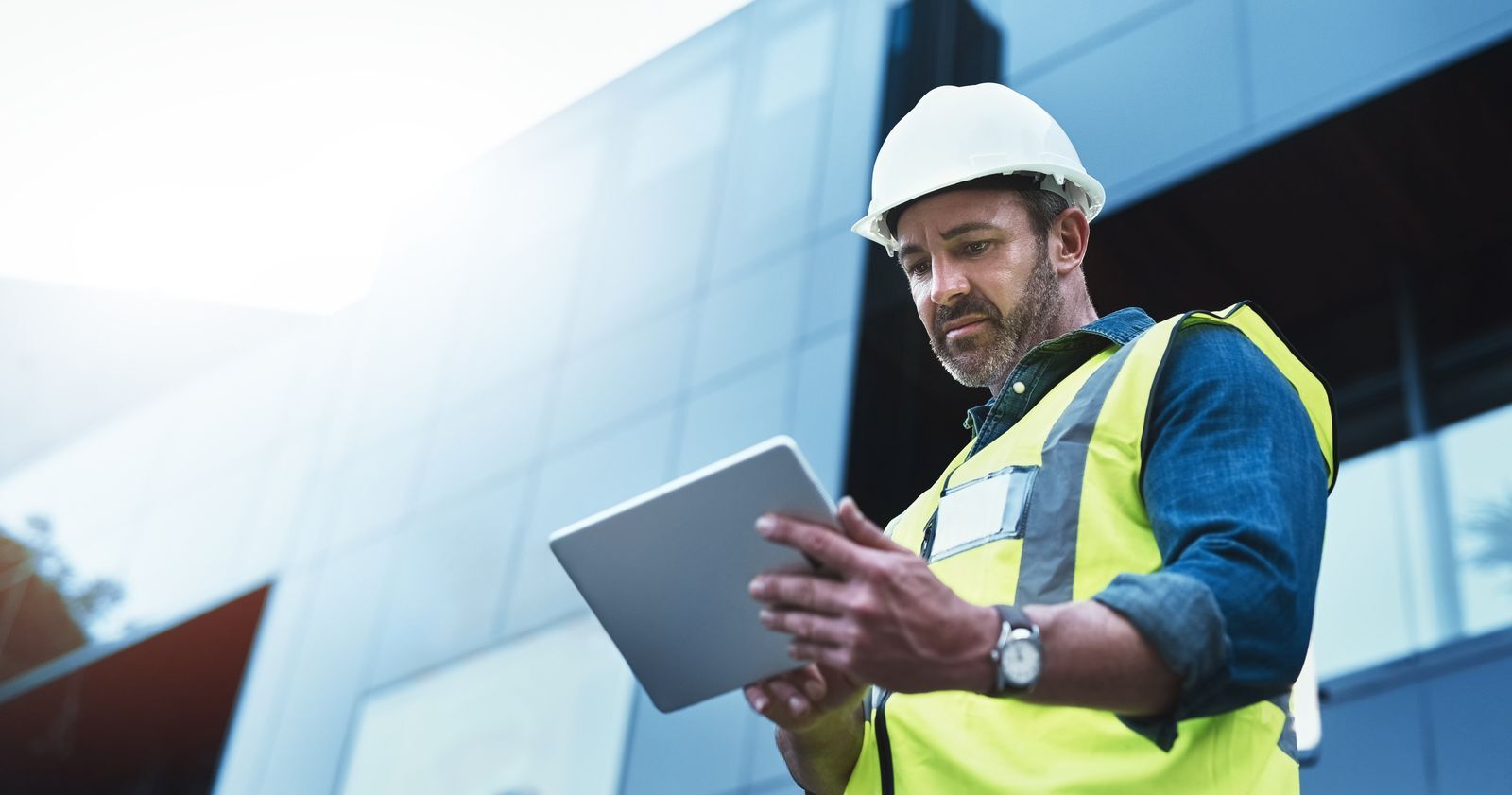Safety professional in PPE reviewing training and inspection records on a tablet at a work site