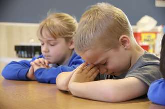 Image of young students praying in class