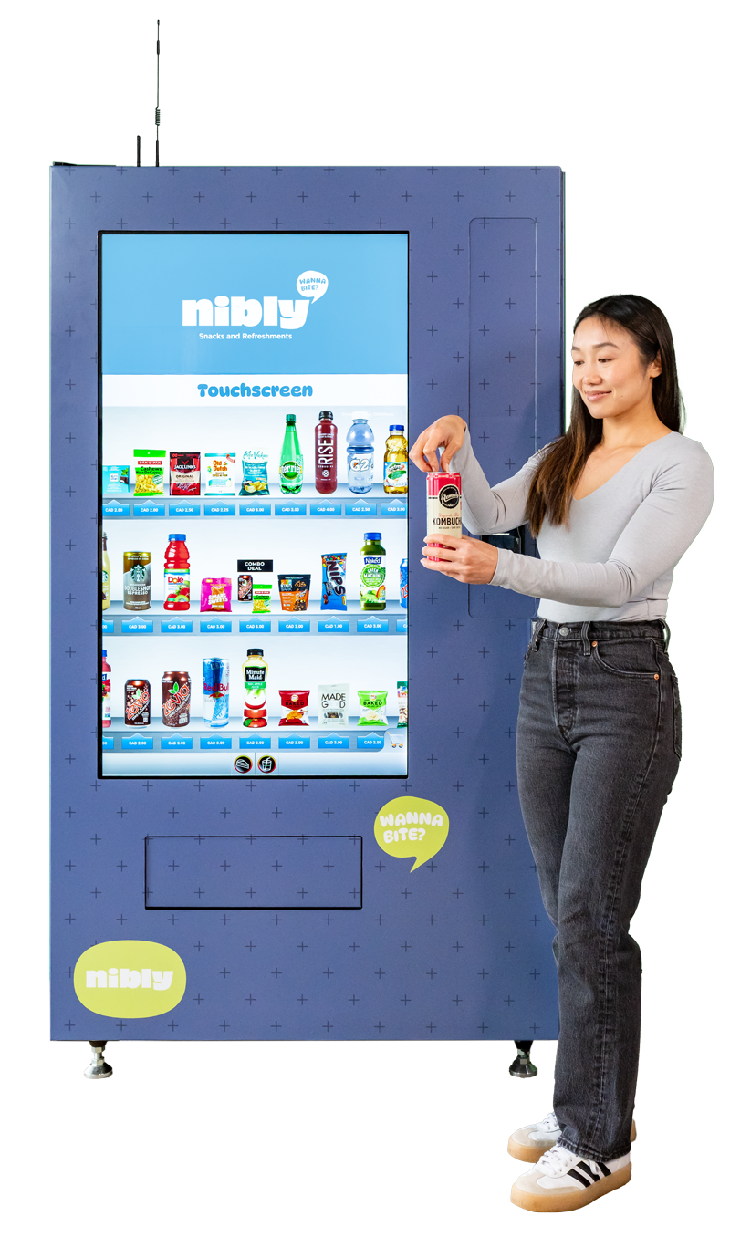Image of Nibly Vending Machine Operator standing beside digital vending machine touch screen with snacks and drink choices displayed while opening a can of Kombucha.