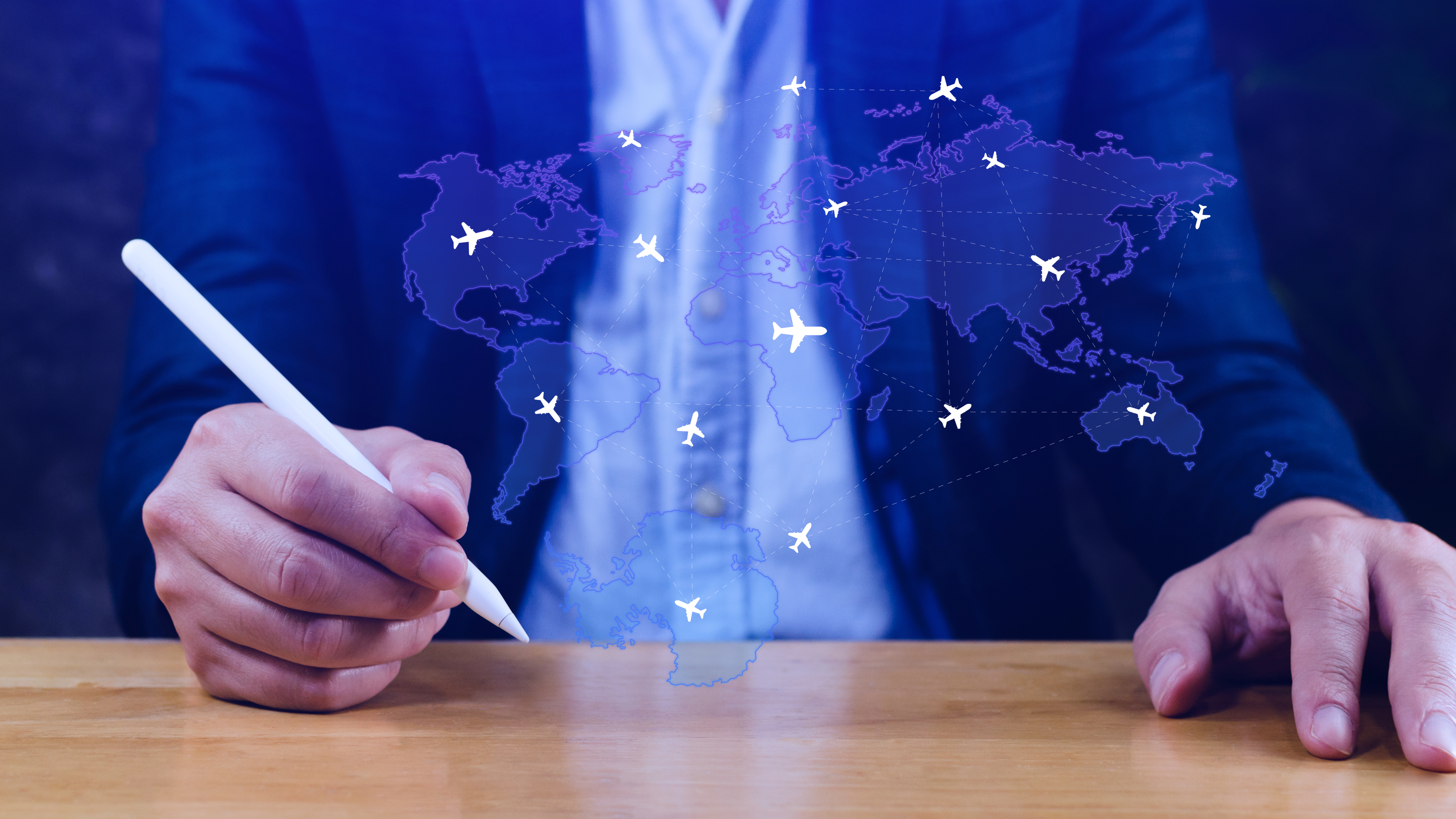 Businessman using a stylus to interact with a digital world map overlaid with airplane icons and flight paths, representing global aviation, logistics, or airline network plannin