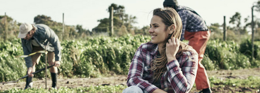 Several people workingi n a field. A woman crouched in the foreground is smiling at something out of frame.