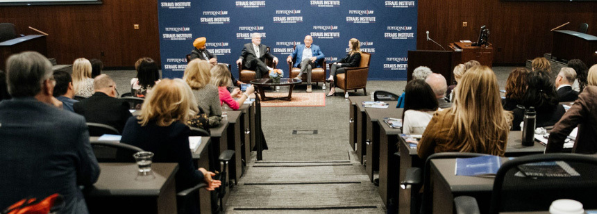 An audience watching a talk between 4 people seated on a stage.