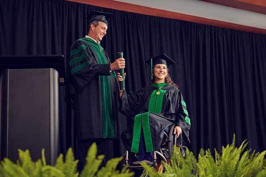 Julia Rodes in a wheelchair on stage at a graduation ceremony receiving her medical degree