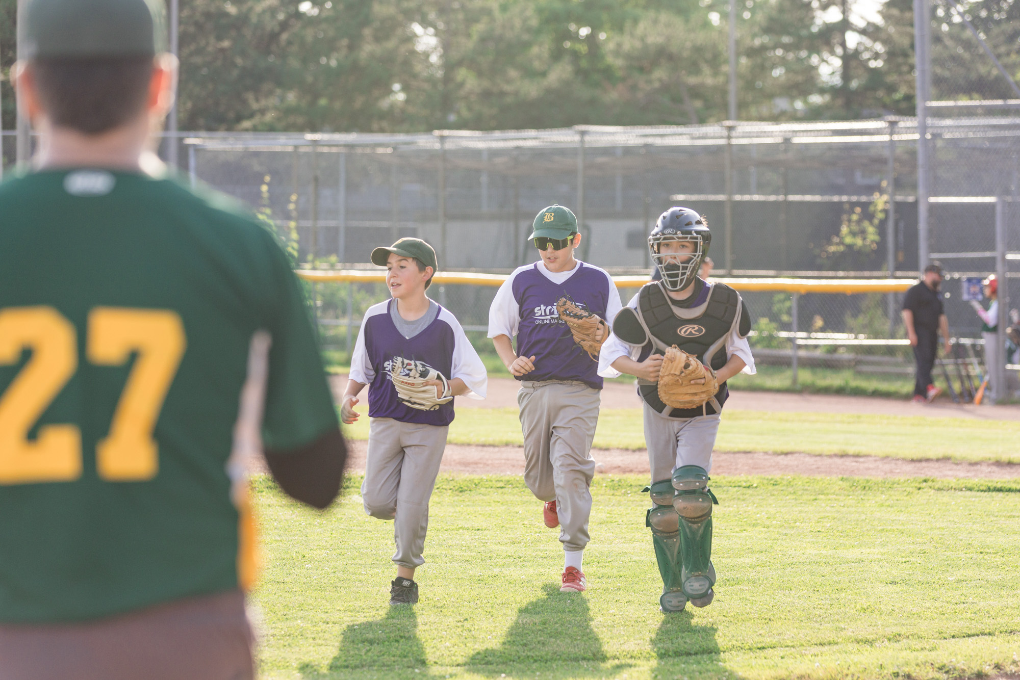 Three young baseball players running across the field during a game