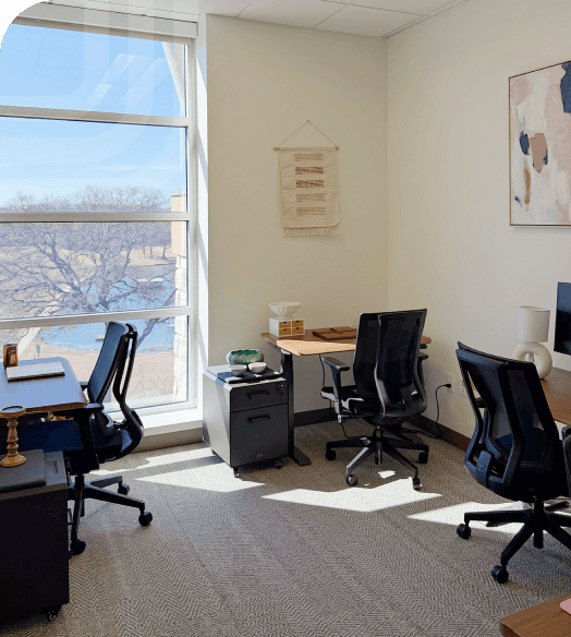 Private office workspace with multiple desks, ergonomic chairs, storage drawers, and a large window with outdoor views.