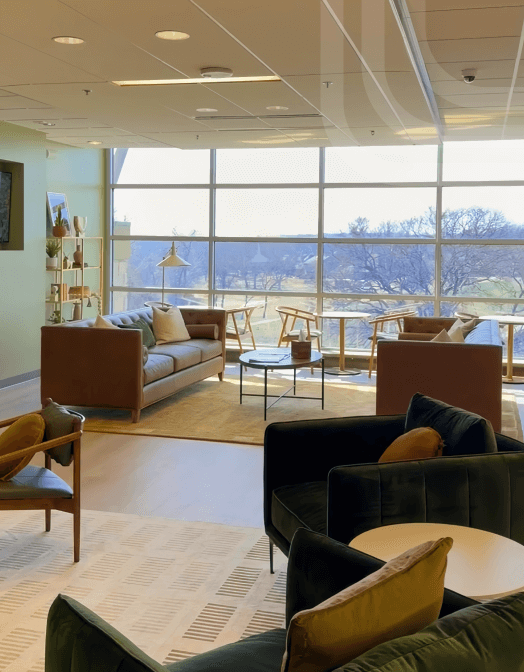 Coworking lounge with sofas, armchairs, coffee tables, and large floor-to-ceiling windows letting in natural light.