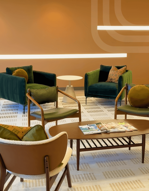Modern seating area with armchairs, a coffee table with magazines, and warm accent lighting on an orange wall.
