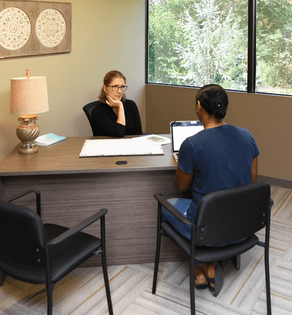Three professionals — two men and one woman — engaged in discussion around a wooden conference table with notepads and pens.