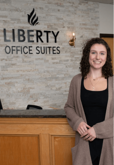 Friendly receptionist greeting a visitor at the front desk of the office suite lobby.