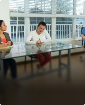 Group of professionals collaborating around a glass conference table in a bright team office with floor-to-ceiling windows.
