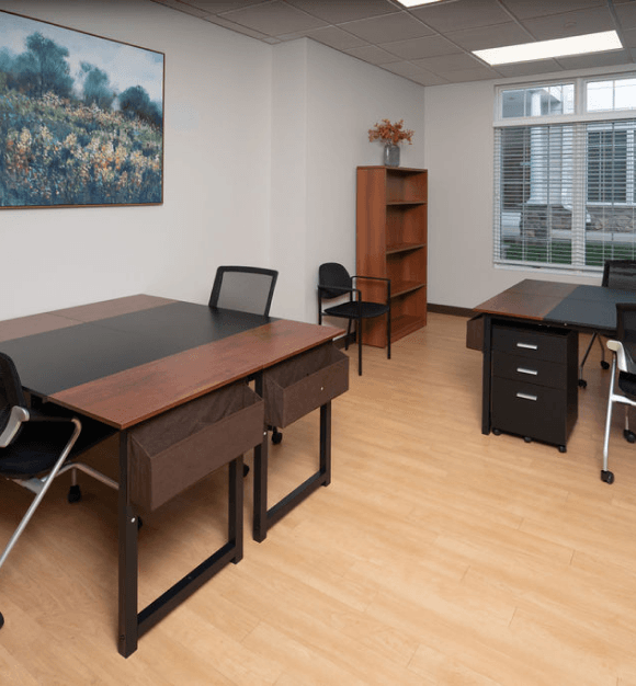 Mid-sized boardroom with a long wooden conference table, black mesh chairs, wall-mounted TV display, and whiteboard.

