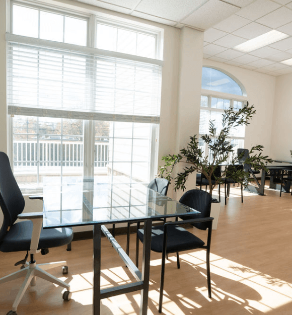 Executive boardroom with a large polished wooden conference table, black leather chairs, wall-mounted flat-screen TV, and framed artwork.