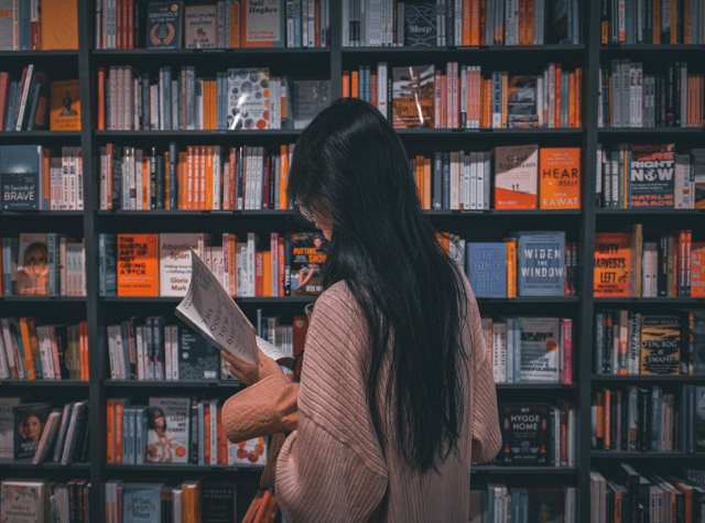 Femme de dos qui lit un livre devant une étagère de bibliothèque