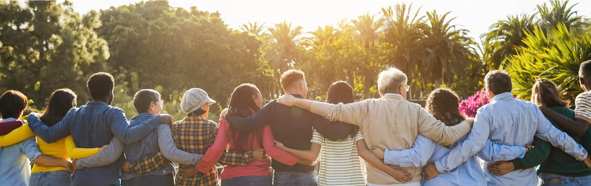 A diverse group of people standing together with their arms around one another outdoors.