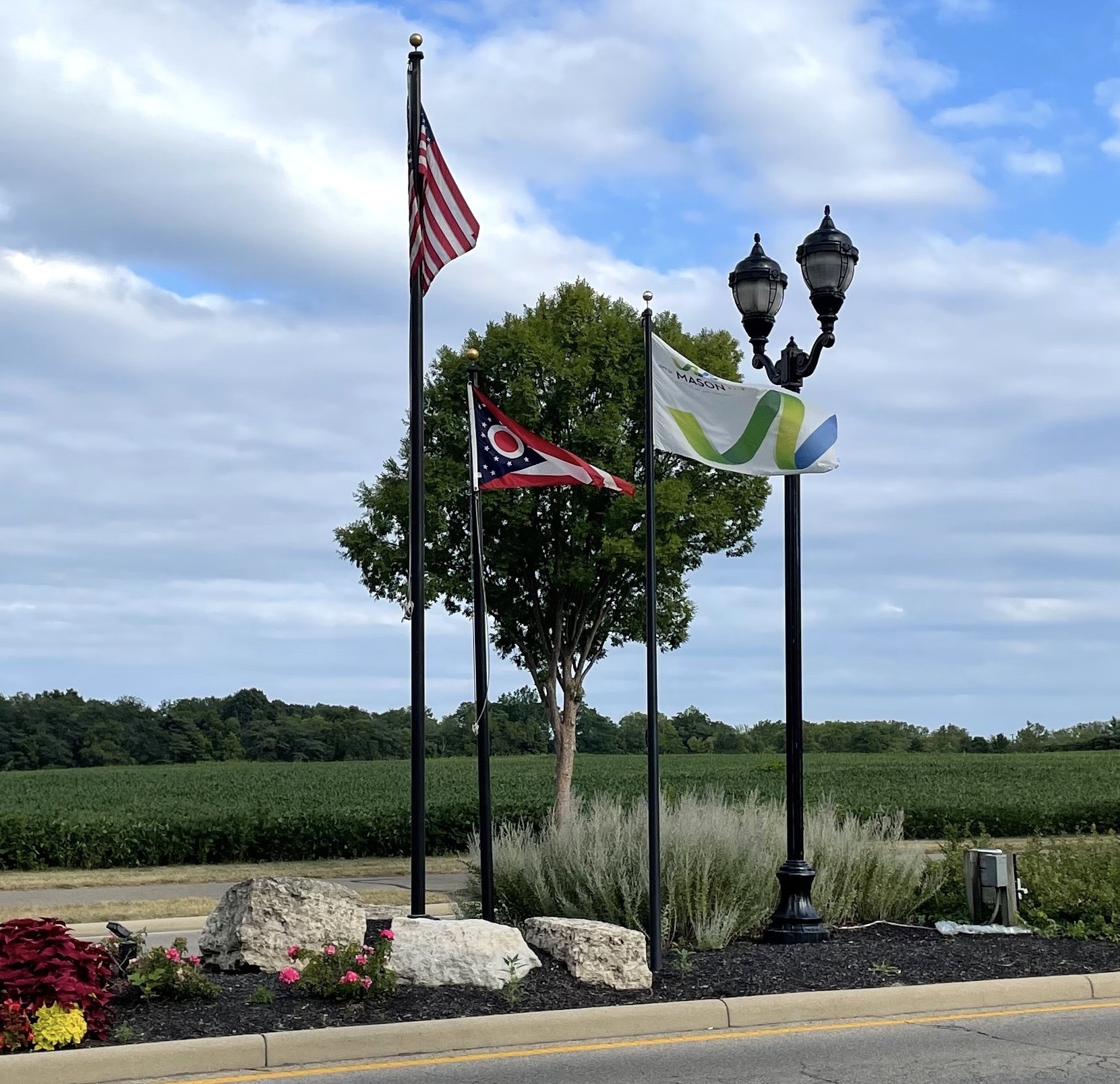 An island on Mason-Montgomery Road with flags of the USA, Ohio, and Mason surrounded by landscaping