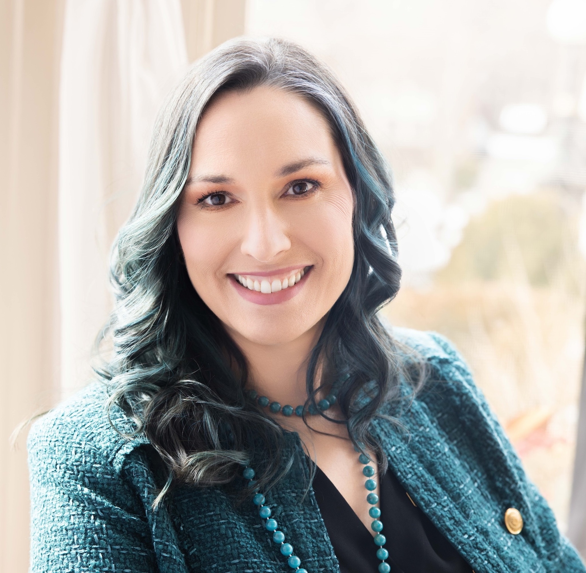 Photo of Joy wearing a woven teal jacket and sitting in front of a window
