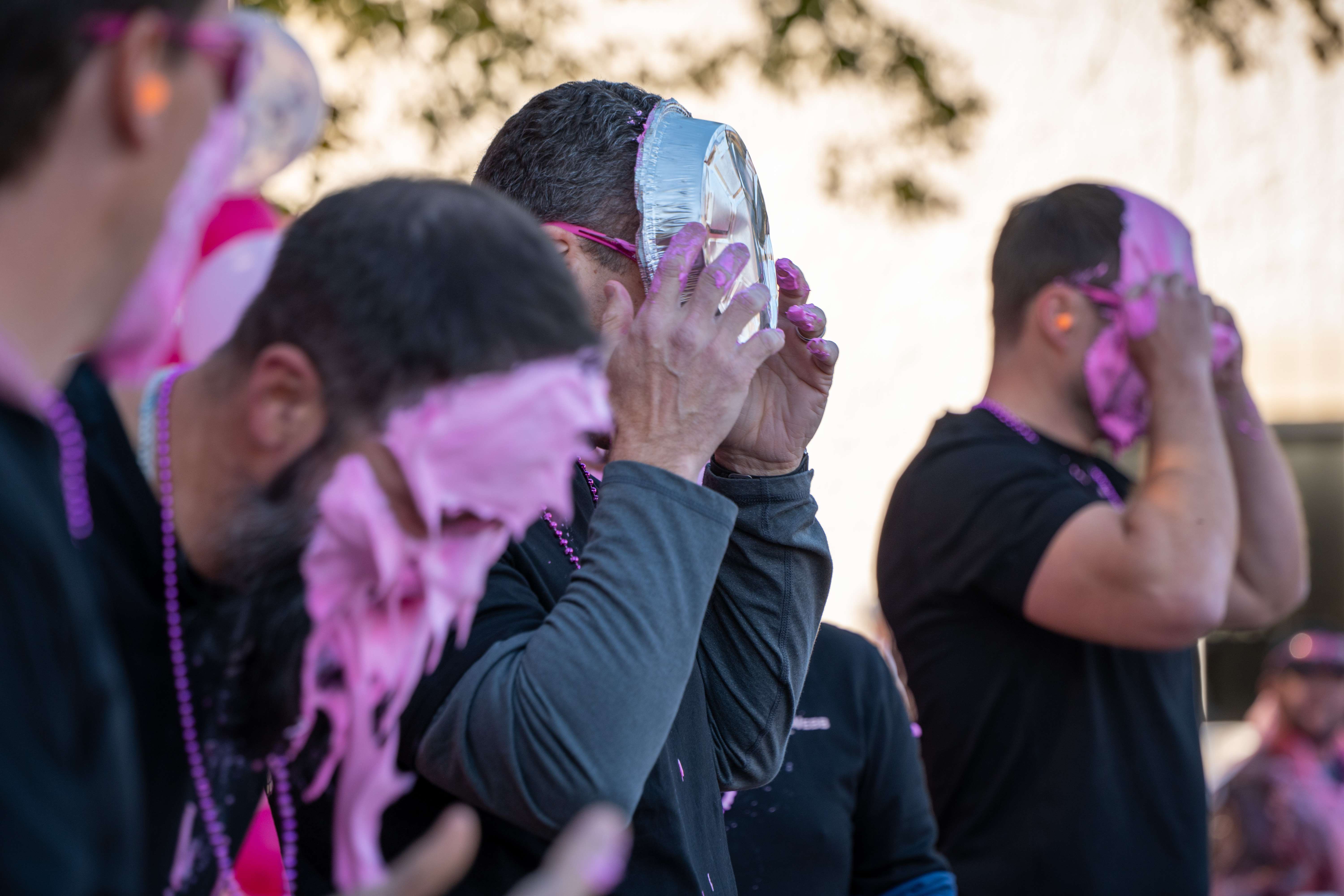 Participants holding pie tins to their faces at Pies for a Cure