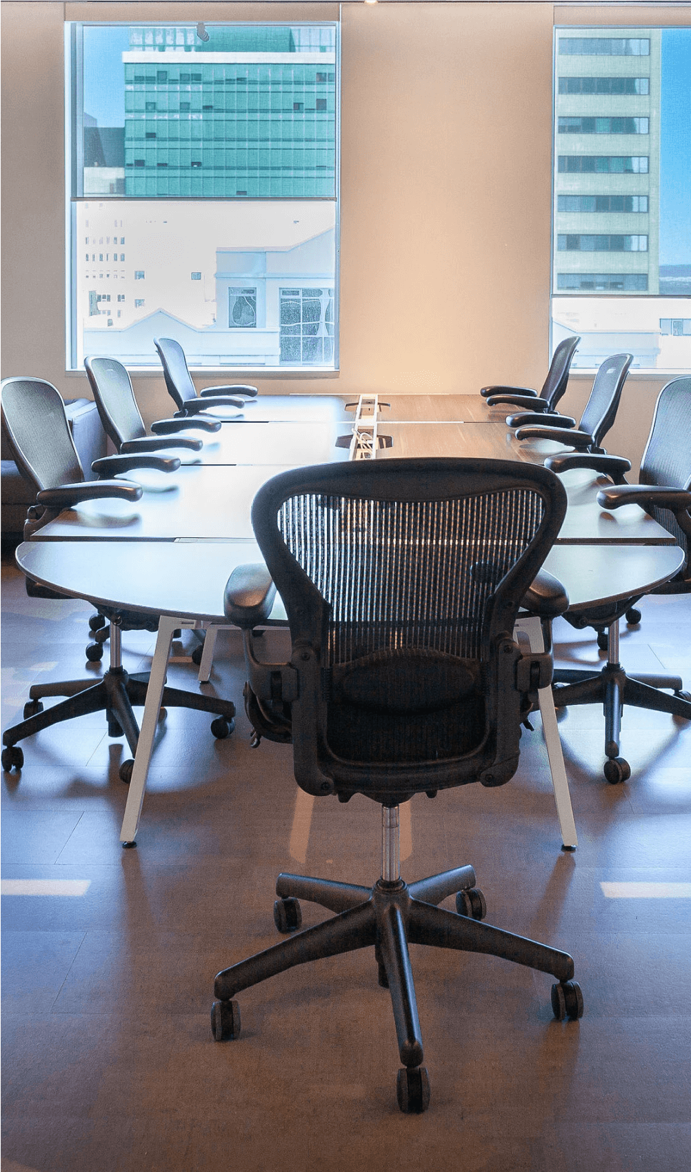 Large meeting room with multiple chairs around a conference-style desk. Outside is visible through large picture windows.