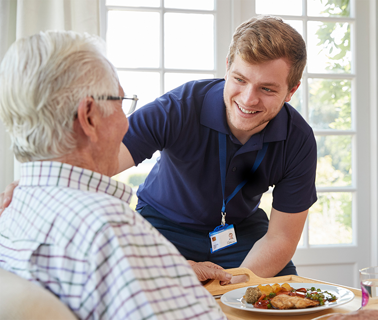 A care person smiling while an elderly resident smiles before enjoying a meal 