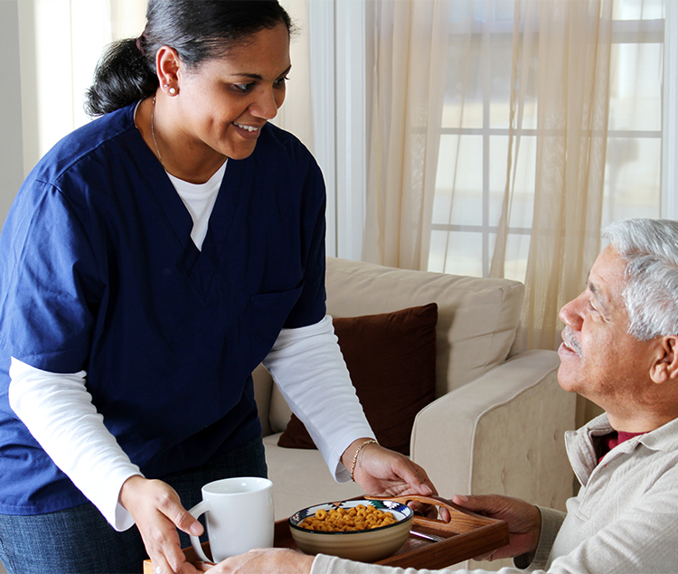 A care person giving an elderly resident their breakfast with a smile 