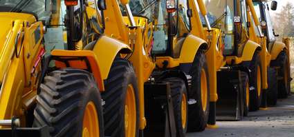 Rij met gele bouwmachines, zoals graaflaadcombinaties, opgesteld voor verkoop of gebruik in de bouwsector.