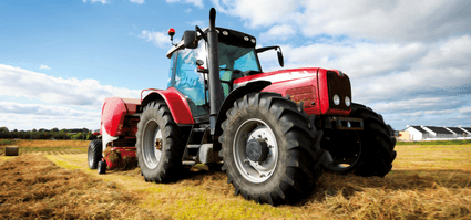 Rode tractor met hooibalenpers op een veld, representatief voor landbouwmachines en agrarisch werk.