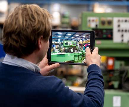 Veilingsadviseur van Troostwijk Auctions  maakt een foto met een tablet van metaalbewerkingsmachines in een werkplaats, representatief voor het documenteren en veilen van industriële apparatuur