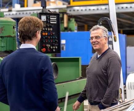 Twee mannen in gesprek bij een groene metaalbewerkingsmachine in een werkplaats, representatief voor industriële verkoop en machineveilingen