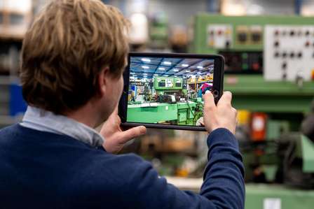 Veilingsadviseur van Troostwijk Auctions  maakt een foto met een tablet van metaalbewerkingsmachines in een werkplaats, representatief voor het documenteren en veilen van industriële apparatuur